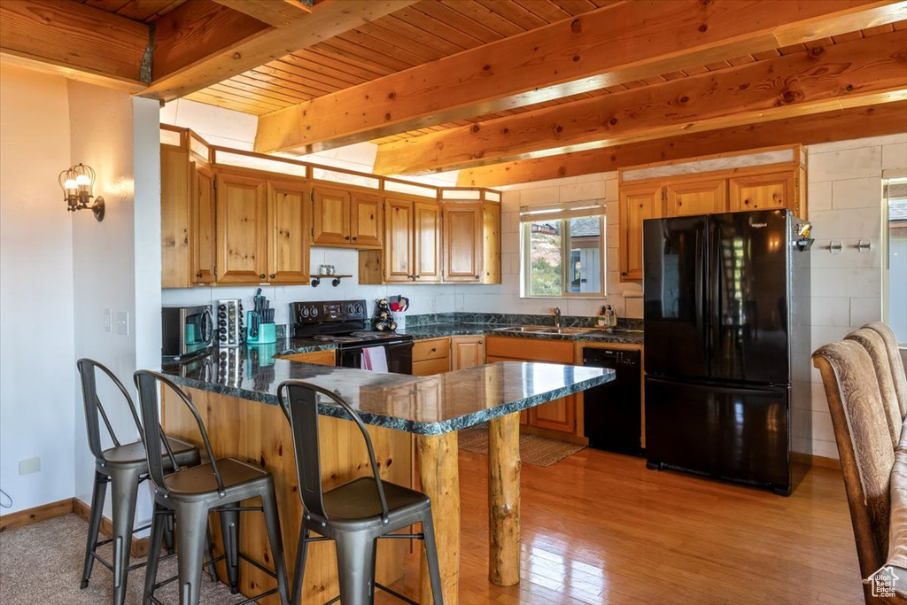 Kitchen with black appliances, sink, kitchen peninsula, light hardwood / wood-style floors, and beam ceiling