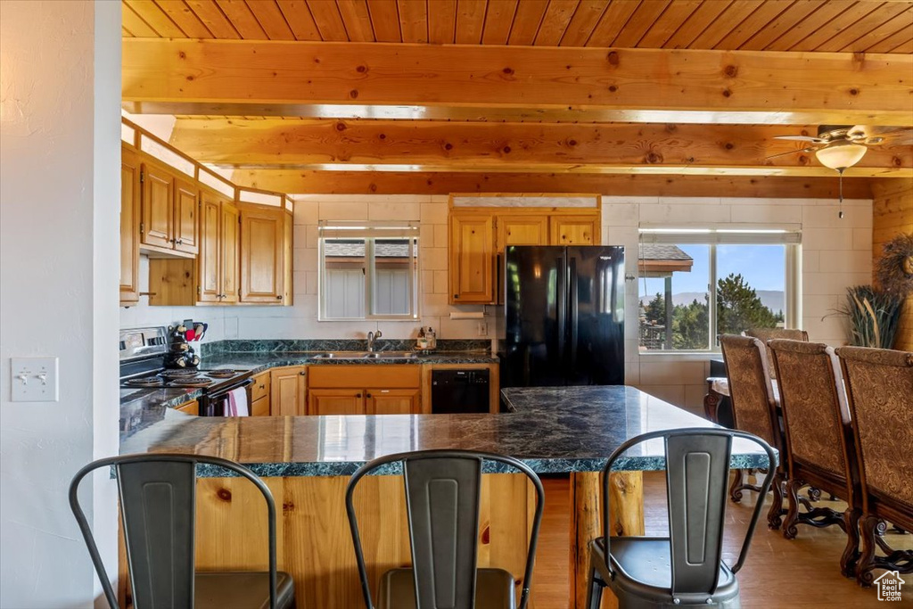 Kitchen featuring a kitchen bar, beamed ceiling, black appliances, sink, and wood-type flooring