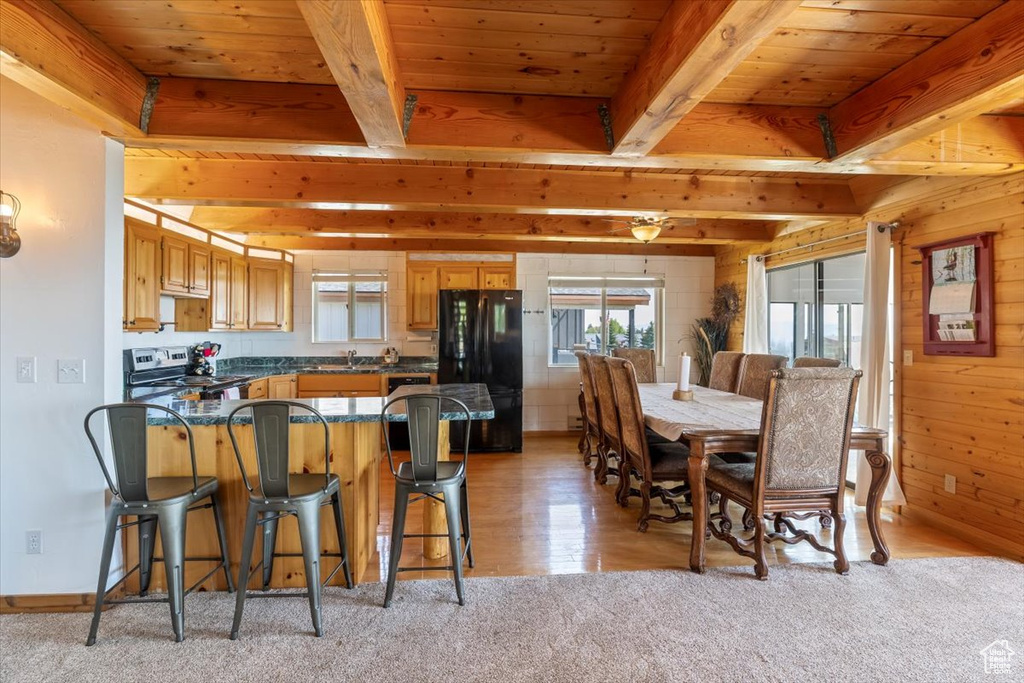 Kitchen with light hardwood / wood-style flooring, beam ceiling, black refrigerator, and stainless steel electric stove