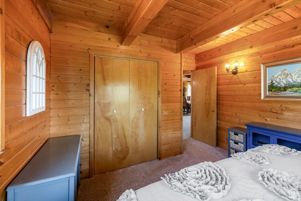 Carpeted bedroom with beam ceiling, wood walls, a closet, and wood ceiling