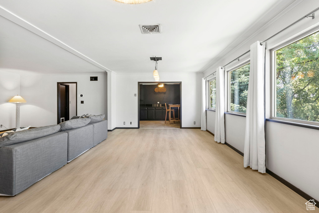 Unfurnished living room featuring plenty of natural light, crown molding, and light hardwood / wood-style floors