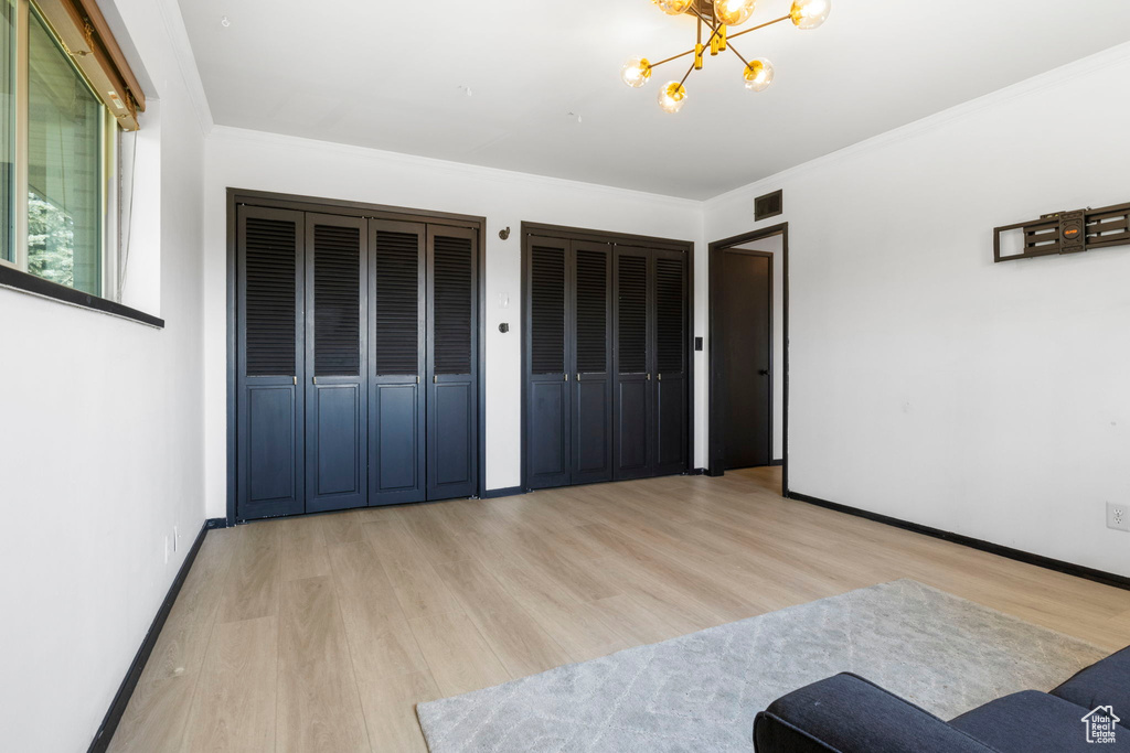 Bedroom with multiple closets, a chandelier, ornamental molding, and light hardwood / wood-style floors