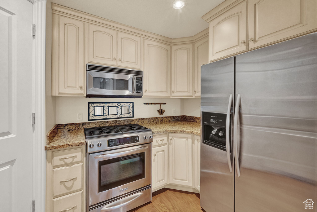 Kitchen featuring cream cabinets, light stone counters, light hardwood / wood-style flooring, and stainless steel appliances