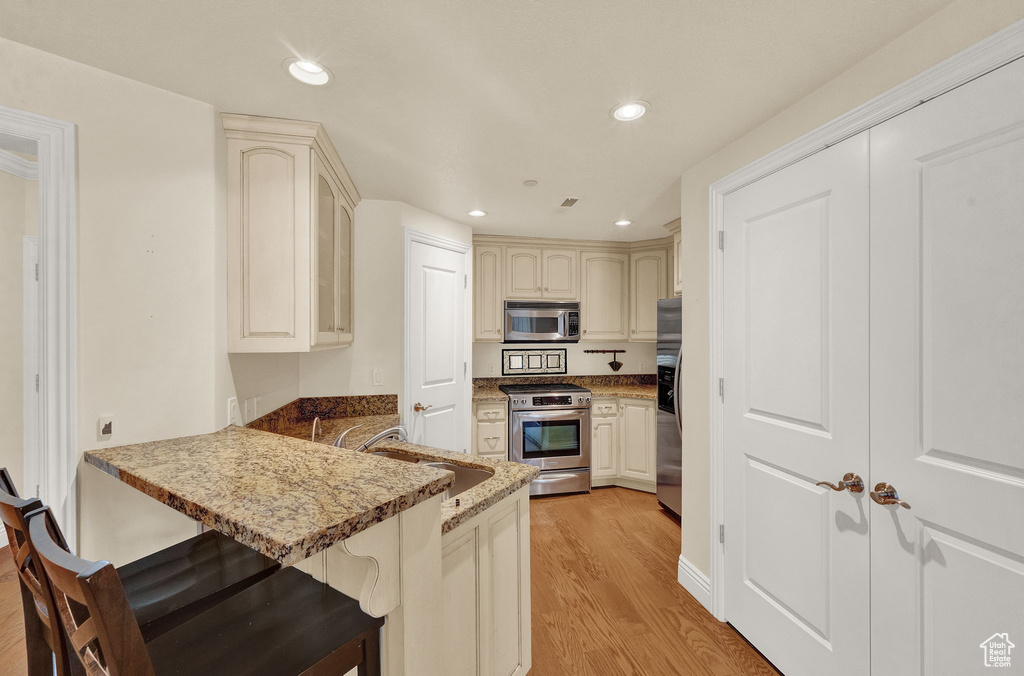 Kitchen featuring kitchen peninsula, stainless steel appliances, light hardwood / wood-style floors, stone counters, and sink