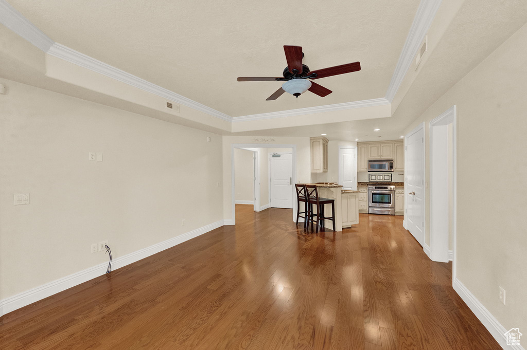 Unfurnished living room featuring hardwood / wood-style flooring, crown molding, and a tray ceiling