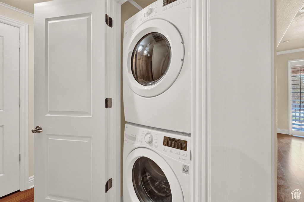 Clothes washing area with stacked washer and clothes dryer, hardwood / wood-style flooring, and ornamental molding