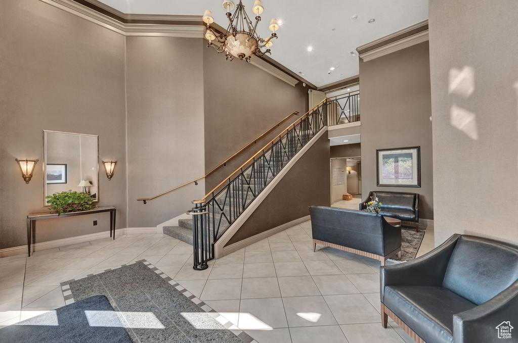 Entryway with crown molding, a towering ceiling, a notable chandelier, and light tile patterned floors