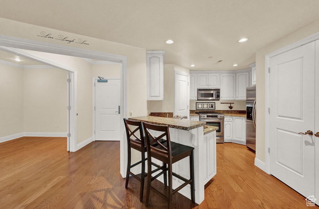 Kitchen with kitchen peninsula, white cabinets, light hardwood / wood-style floors, appliances with stainless steel finishes, and stone countertops