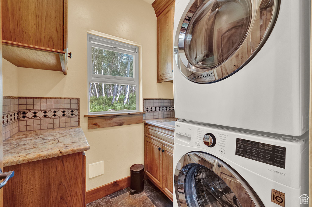 Laundry room with stacked washer / dryer, cabinets, and dark tile patterned flooring