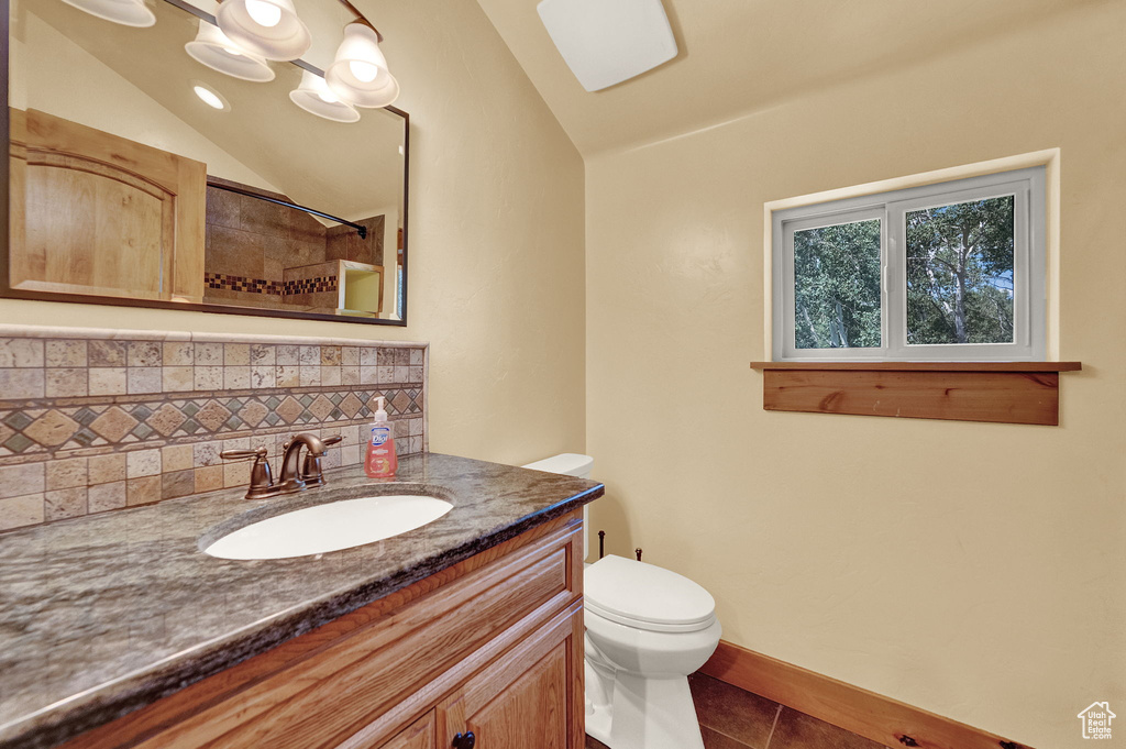 Bathroom with tasteful backsplash, lofted ceiling, tile patterned floors, toilet, and vanity