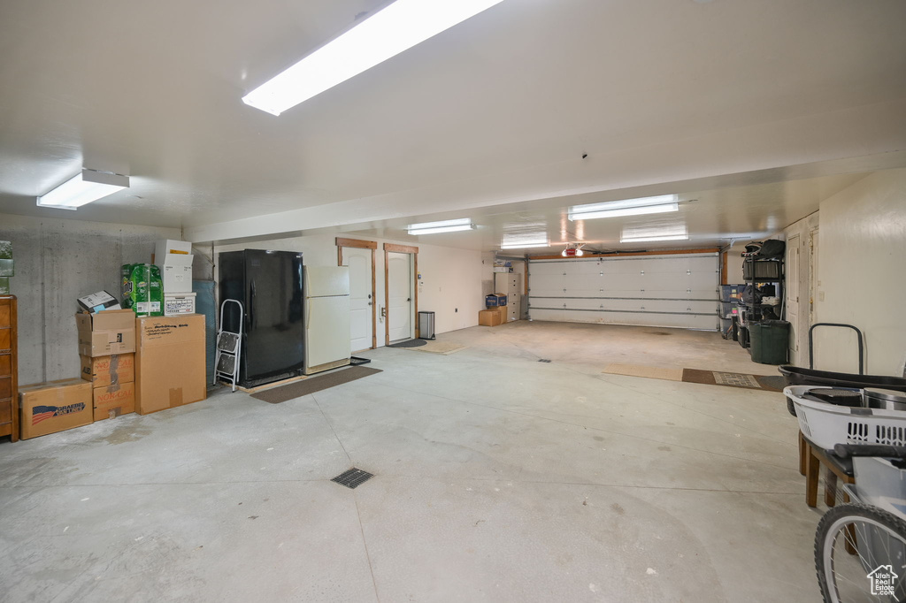 Garage with black refrigerator with ice dispenser and white fridge