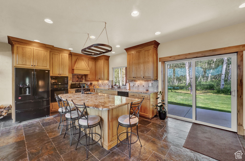 Kitchen featuring decorative backsplash, a kitchen island with sink, black appliances, and a healthy amount of sunlight