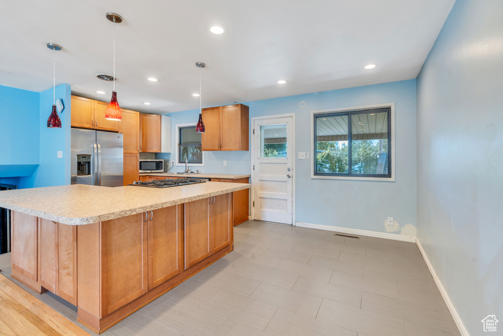 Kitchen with sink, hanging light fixtures, a kitchen island, light tile patterned floors, and stainless steel appliances