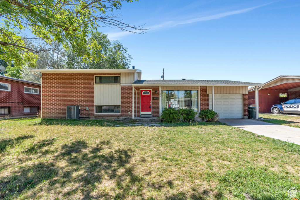 Split level home featuring central AC unit, a front yard, and a garage