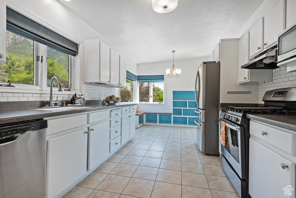 Kitchen featuring hanging light fixtures, appliances with stainless steel finishes, white cabinetry, and backsplash