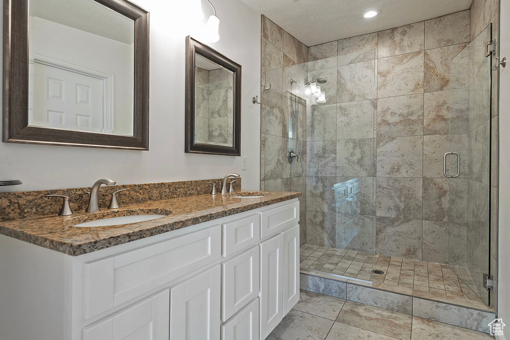 Bathroom with dual vanity, a shower with door, and tile patterned flooring