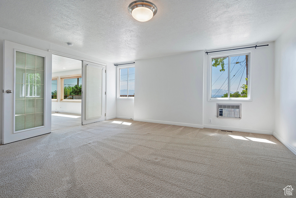 Empty room with light carpet, an AC wall unit, and a textured ceiling