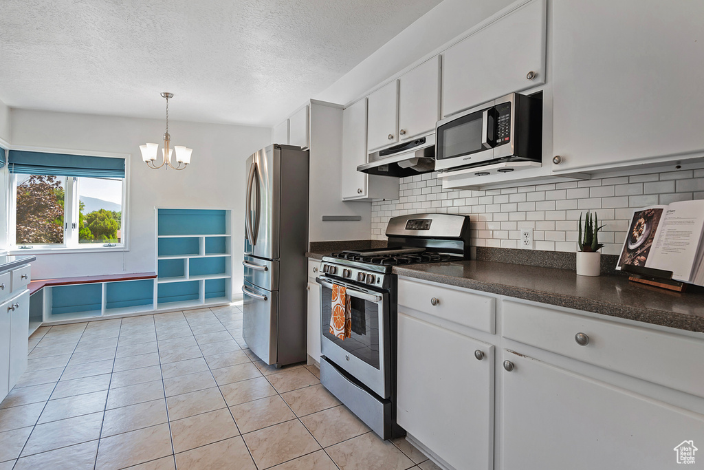 Kitchen featuring appliances with stainless steel finishes, white cabinets, pendant lighting, decorative backsplash, and a textured ceiling