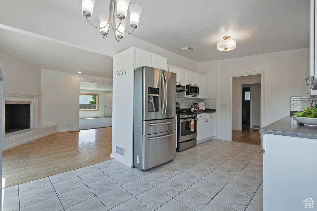 Kitchen with a notable chandelier, white cabinetry, tasteful backsplash, stainless steel appliances, and light hardwood / wood-style flooring