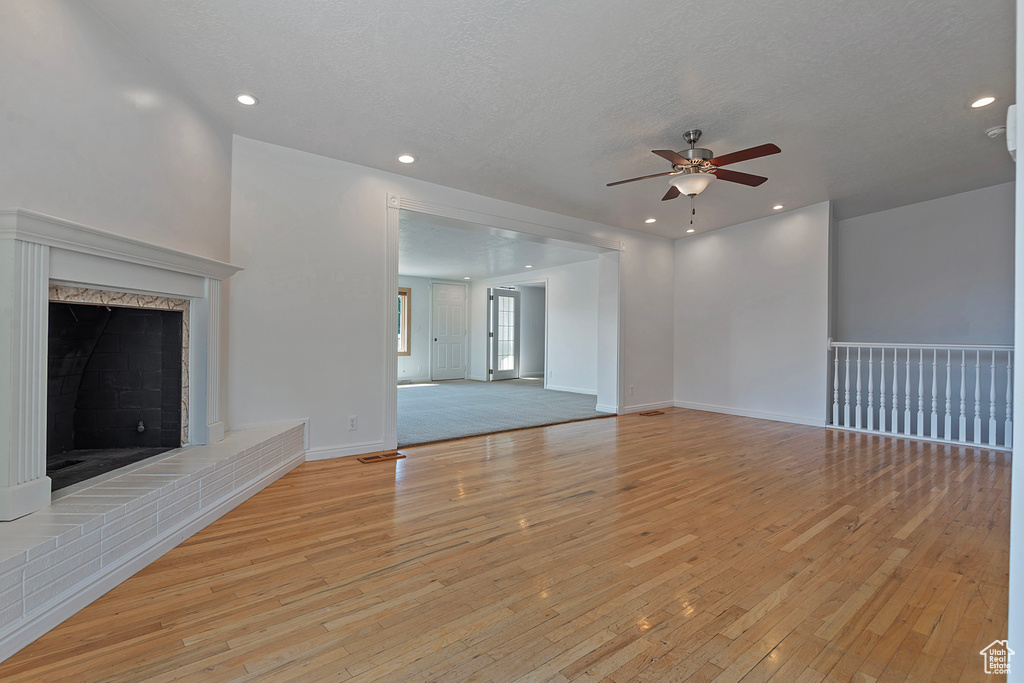 Unfurnished living room with ceiling fan, a textured ceiling, a brick fireplace, and light hardwood / wood-style floors