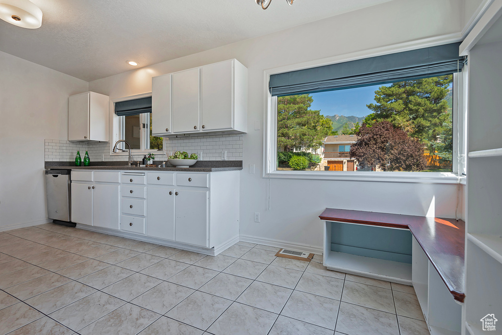 Kitchen with tasteful backsplash, sink, light tile patterned floors, stainless steel dishwasher, and white cabinetry