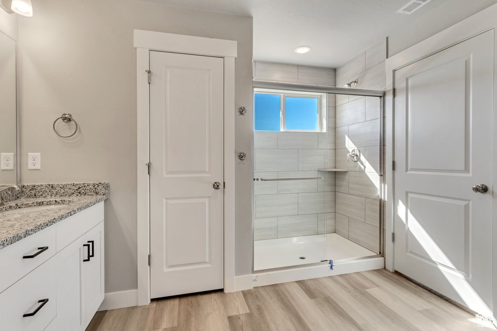 Bathroom with a shower with shower door, hardwood / wood-style floors, and vanity