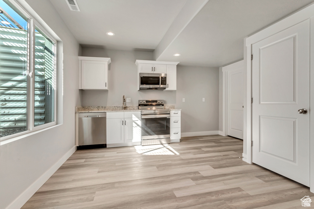 Kitchen featuring stainless steel appliances, sink, light stone counters, light hardwood / wood-style floors, and white cabinetry