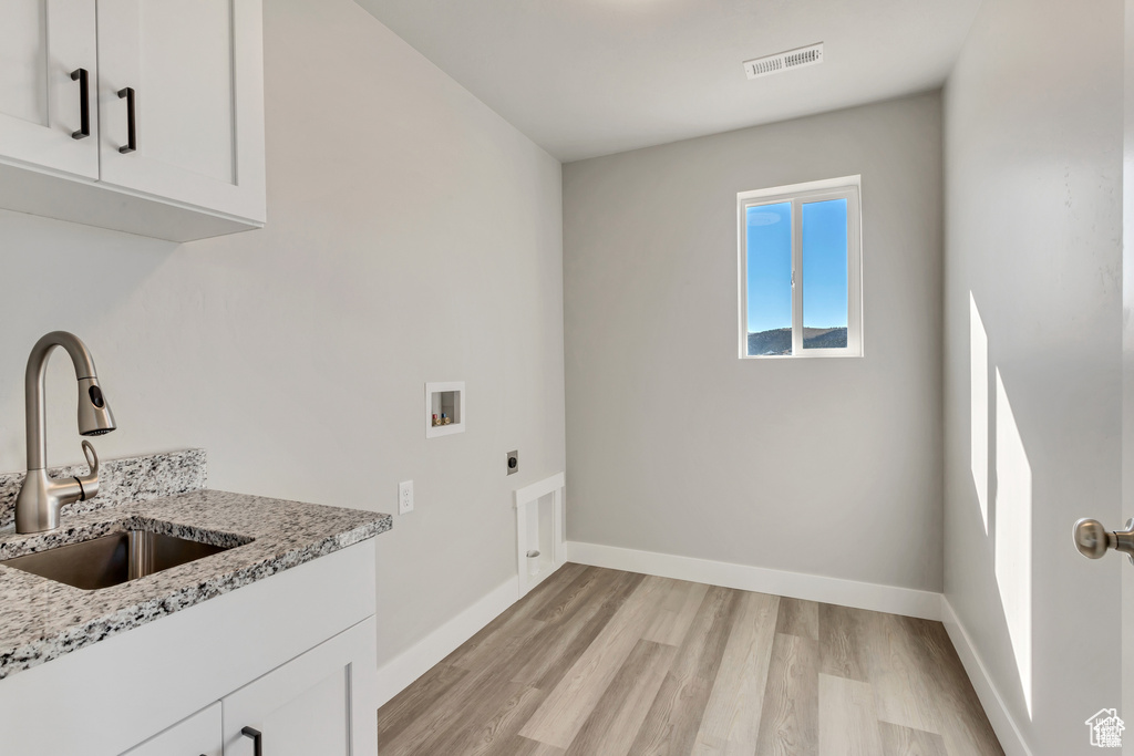 Clothes washing area with light hardwood / wood-style flooring, hookup for a washing machine, sink, cabinets, and hookup for an electric dryer