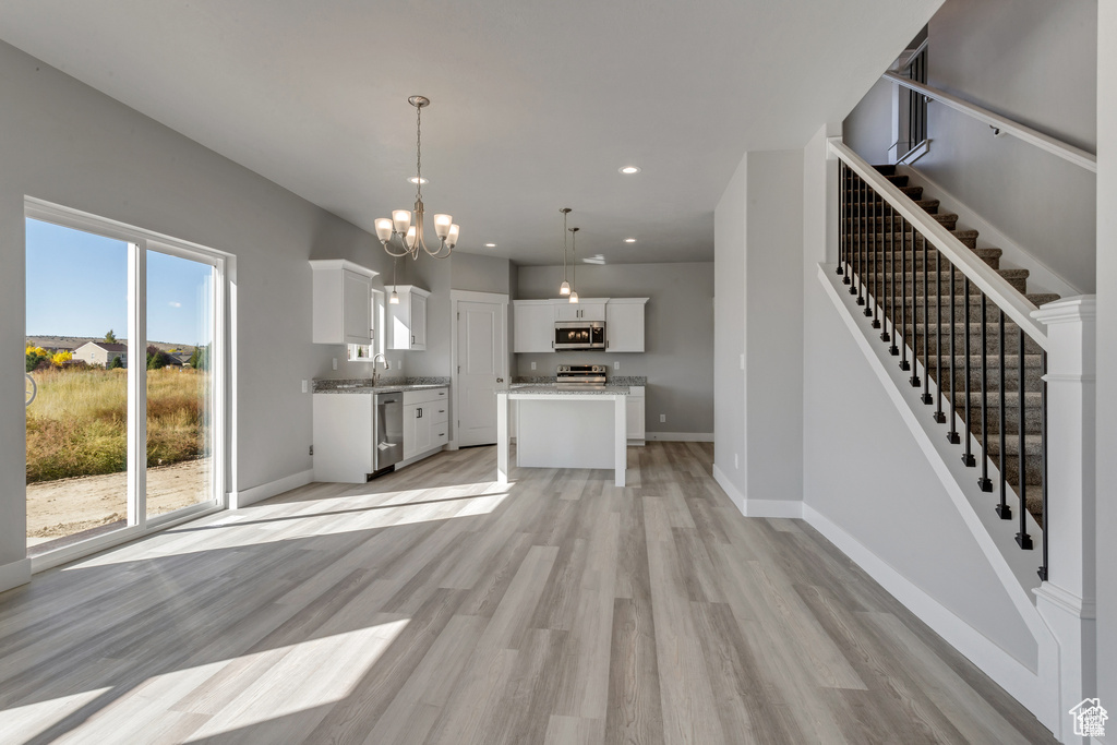 Unfurnished living room with sink, light wood-type flooring, and an inviting chandelier