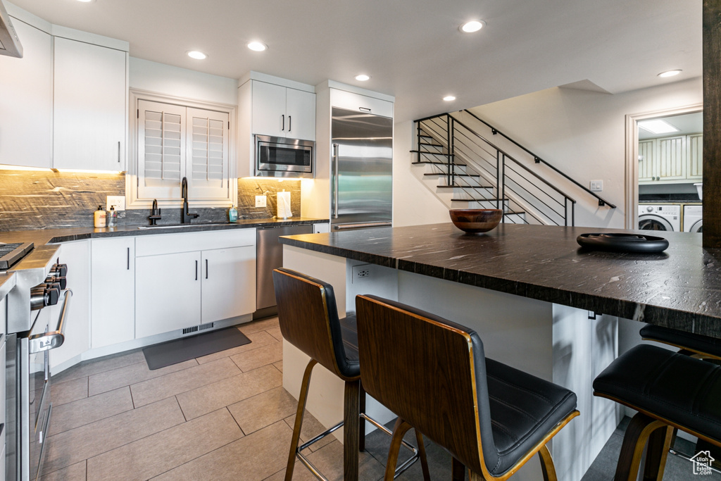 Kitchen featuring white cabinetry, light tile patterned floors, independent washer and dryer, built in appliances, and decorative backsplash