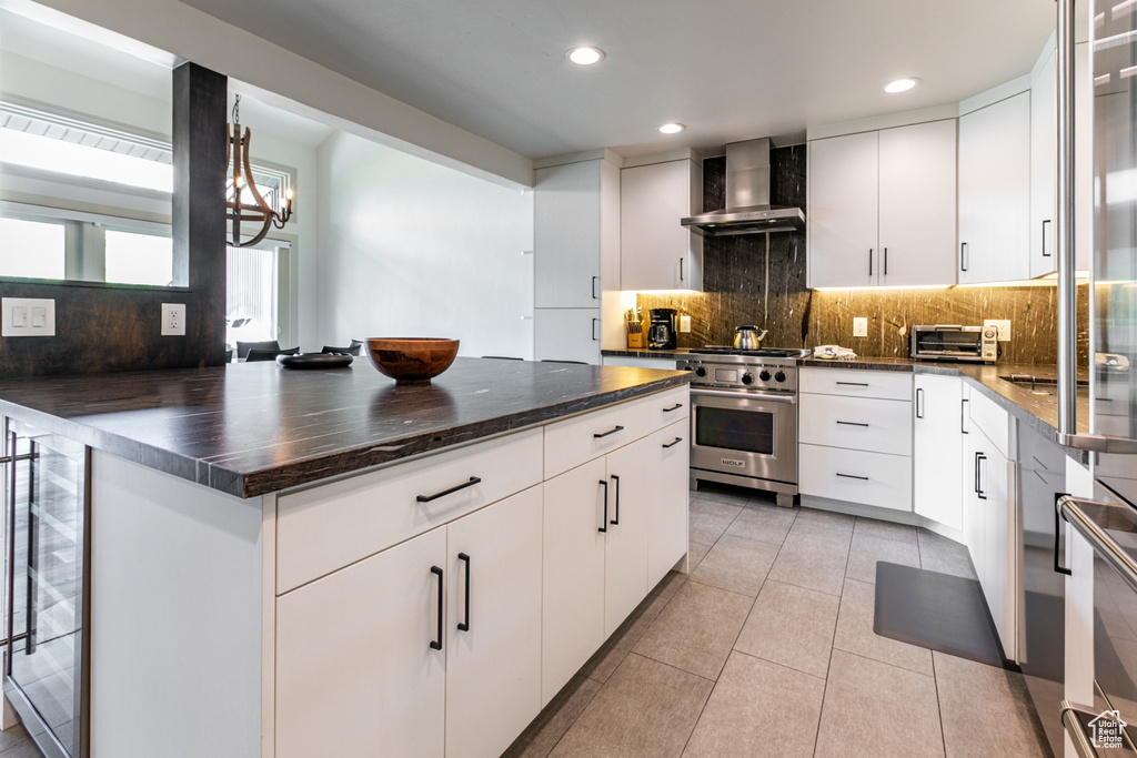 Kitchen featuring white cabinets, wall chimney range hood, backsplash, light tile patterned floors, and high end range