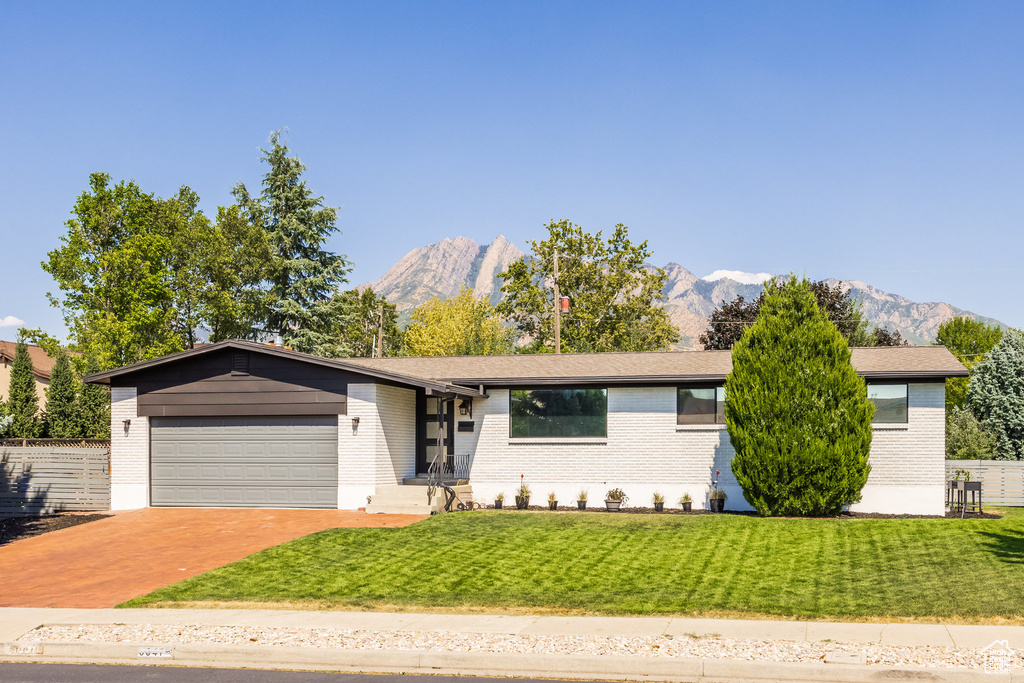 Ranch-style home featuring a mountain view, a garage, and a front lawn