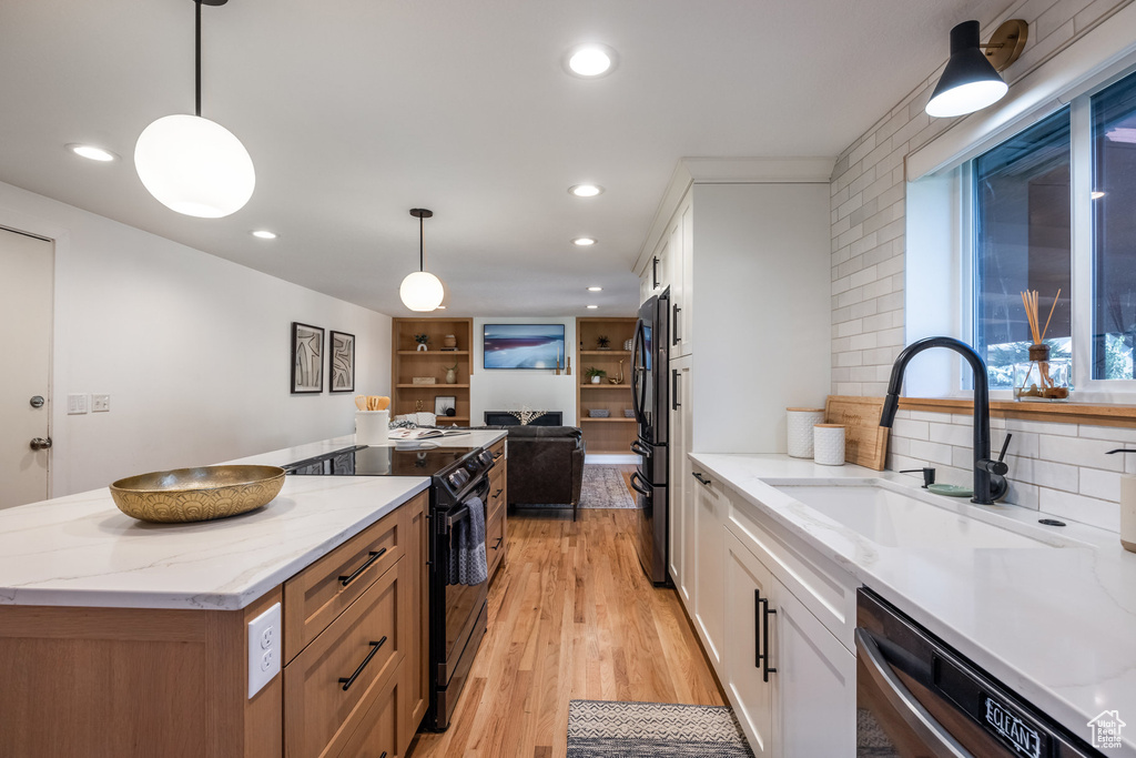 Kitchen featuring light hardwood / wood-style flooring, white cabinets, light stone counters, black appliances, and sink