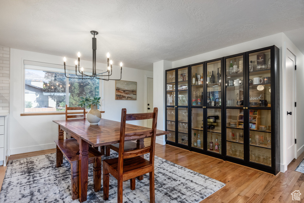 Dining room with brick wall, a textured ceiling, a notable chandelier, and light hardwood / wood-style floors