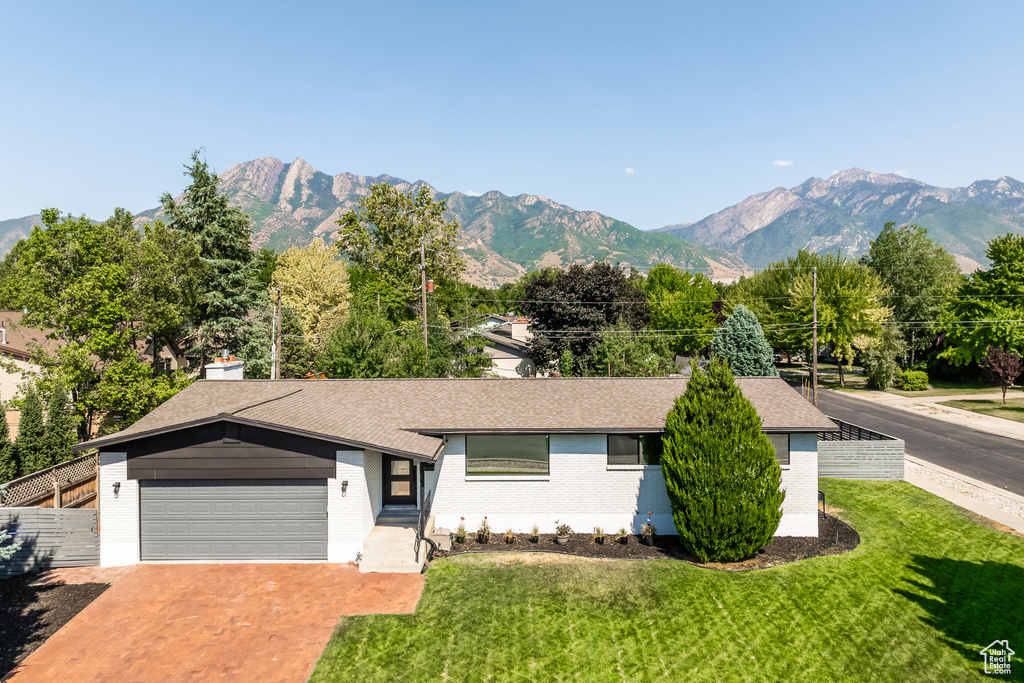 Ranch-style home with a garage, a mountain view, and a front lawn