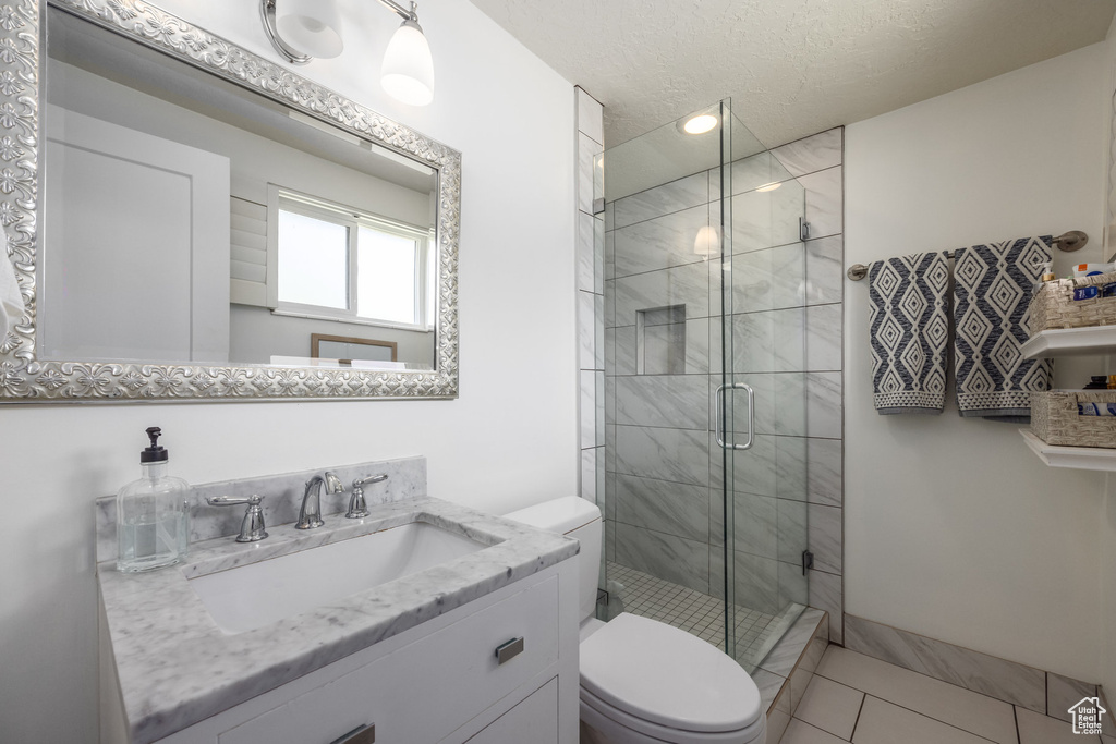 Bathroom featuring tile patterned flooring, a textured ceiling, an enclosed shower, toilet, and vanity