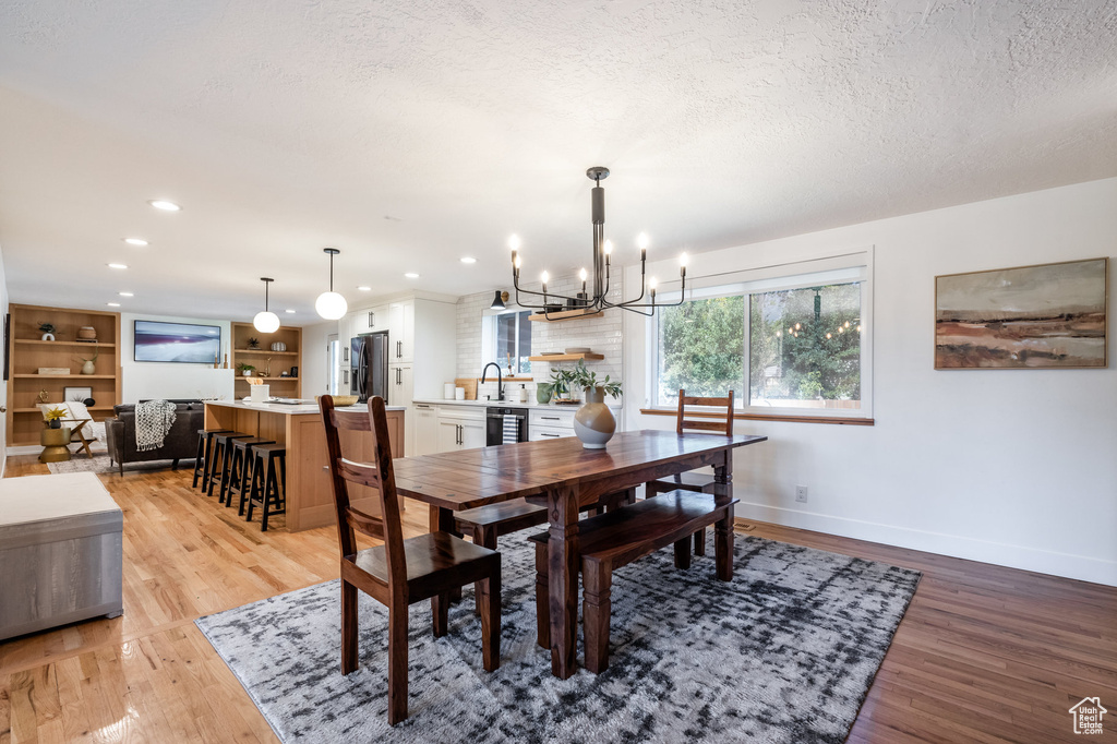 Dining room featuring light hardwood / wood-style flooring, a chandelier, a textured ceiling, beverage cooler, and sink