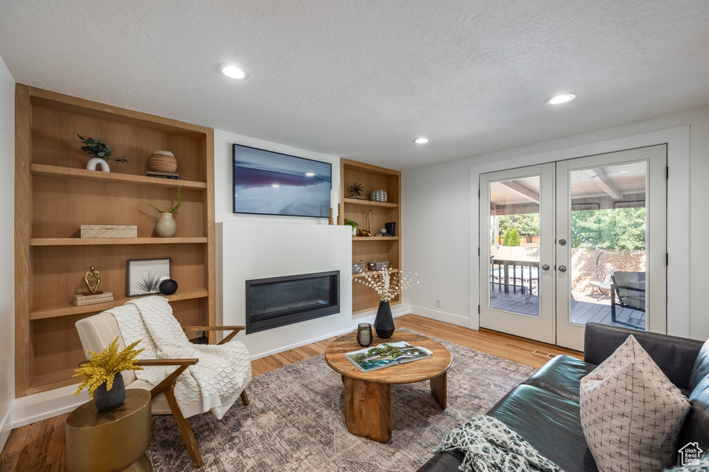 Living room with light hardwood / wood-style floors, built in shelves, french doors, and a textured ceiling