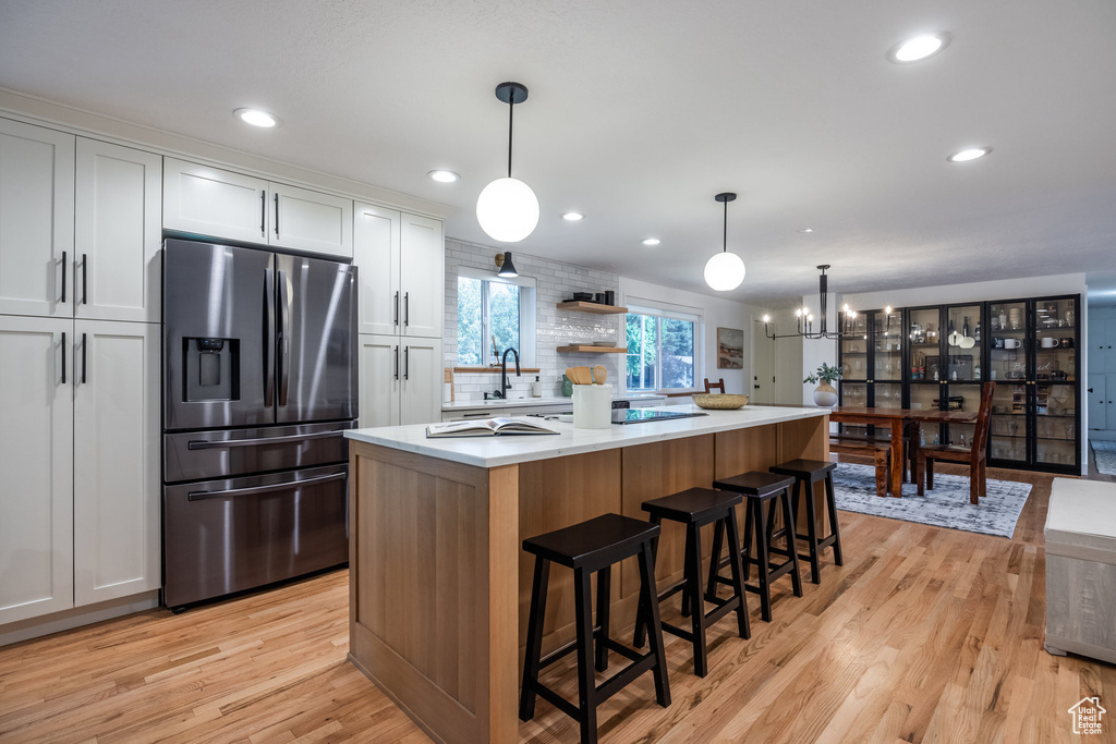 Kitchen with stainless steel fridge with ice dispenser, white cabinetry, light hardwood / wood-style flooring, a kitchen island, and hanging light fixtures