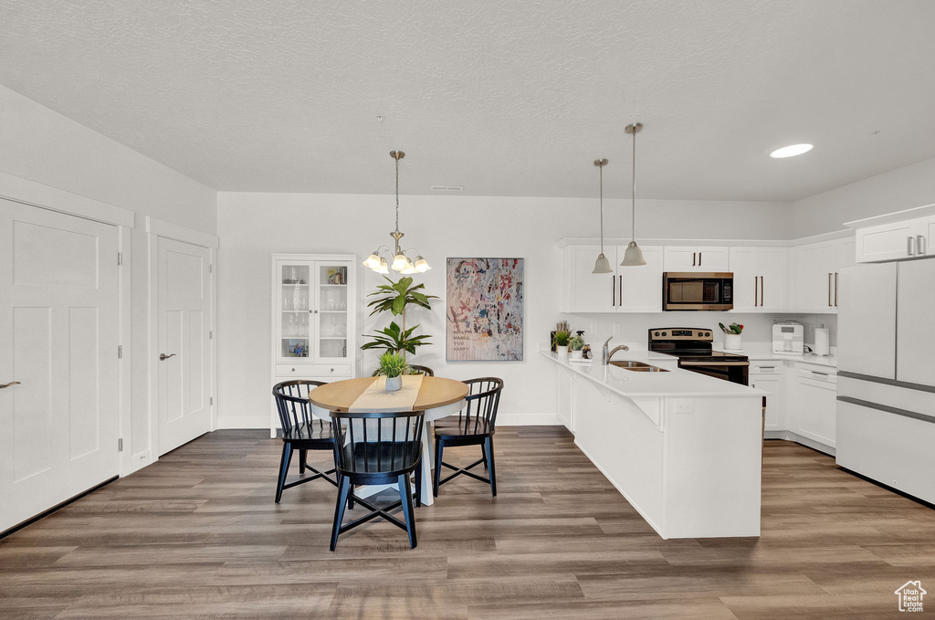 Kitchen with a chandelier, stainless steel appliances, hardwood / wood-style floors, pendant lighting, and sink