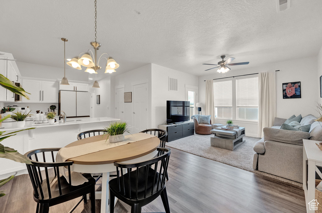 Dining room with ceiling fan with notable chandelier, wood-type flooring, and a textured ceiling