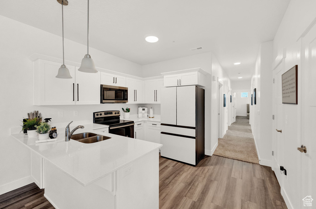 Kitchen featuring white cabinetry, pendant lighting, sink, carpet floors, and appliances with stainless steel finishes