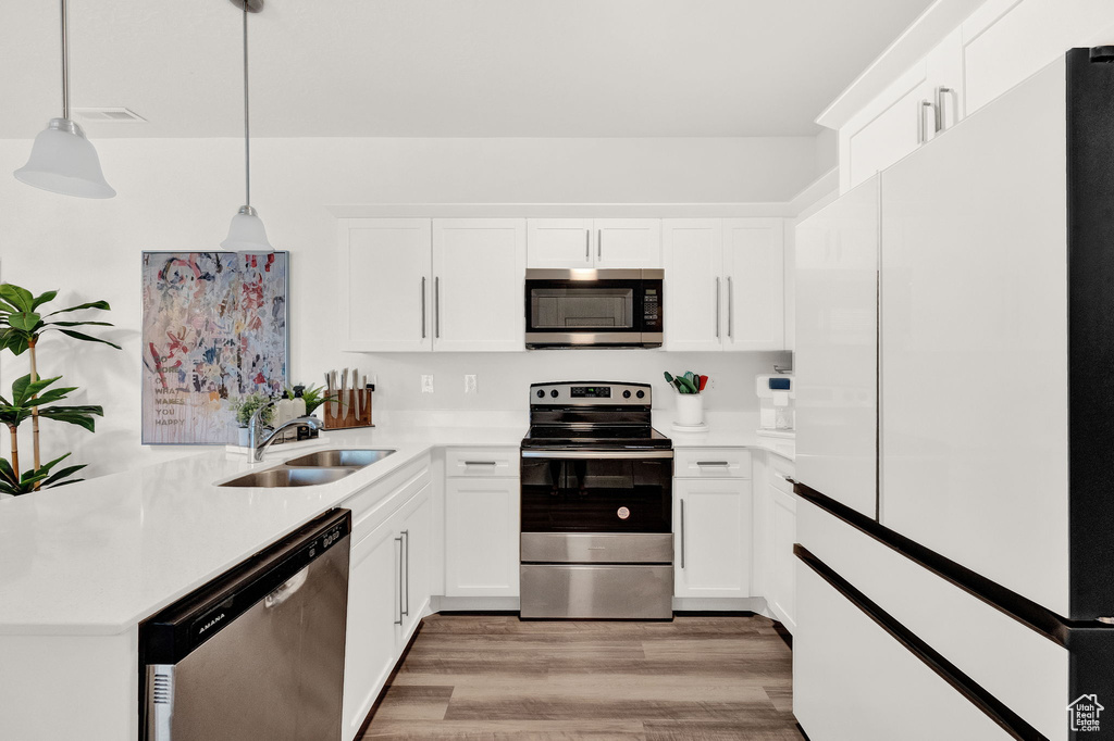 Kitchen featuring hanging light fixtures, white cabinets, light wood-type flooring, sink, and appliances with stainless steel finishes