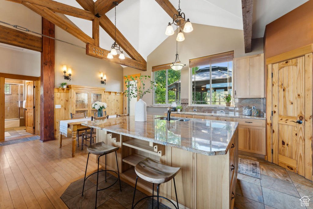 Kitchen with wood-type flooring, a spacious island, light stone counters, and high vaulted ceiling