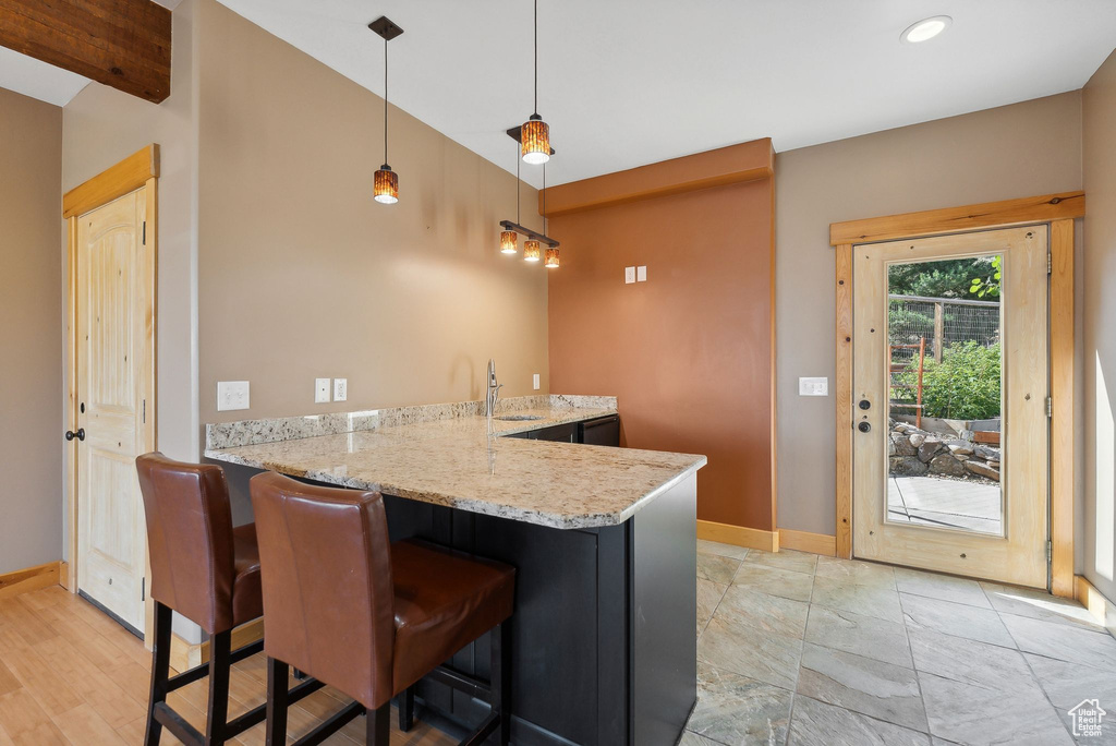 Kitchen featuring a breakfast bar area, kitchen peninsula, light hardwood / wood-style floors, light stone countertops, and decorative light fixtures