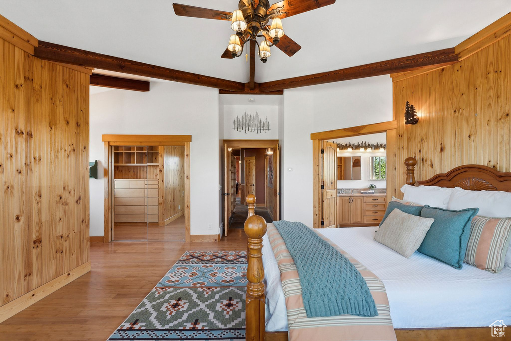 Bedroom with connected bathroom, ceiling fan, hardwood / wood-style floors, beamed ceiling, and wood walls