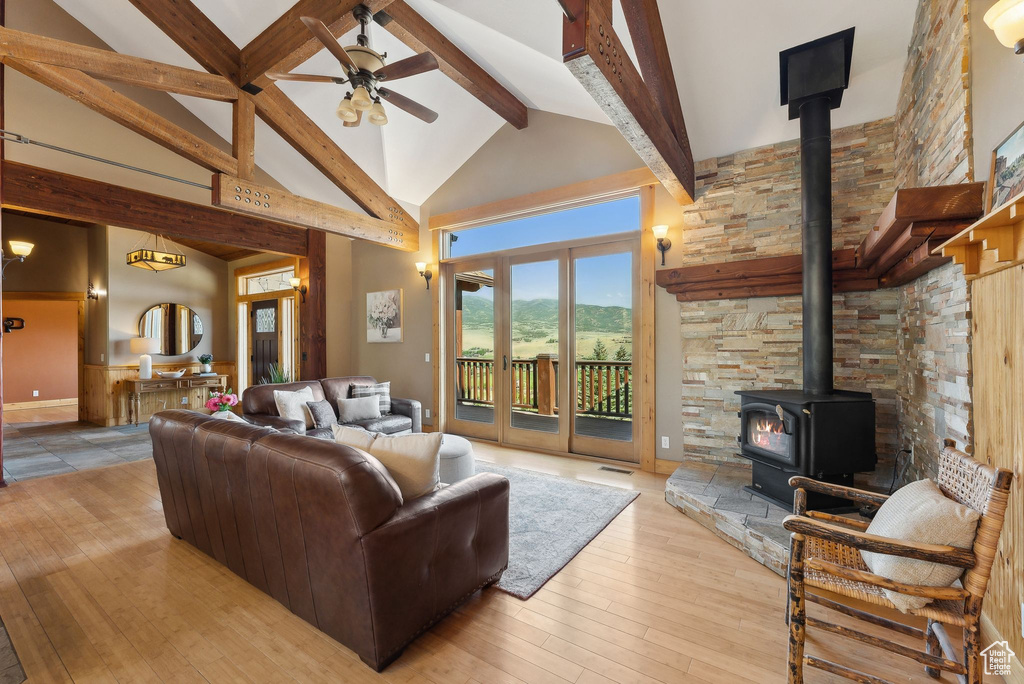 Living room featuring a wood stove, ceiling fan, light hardwood / wood-style floors, beamed ceiling, and high vaulted ceiling