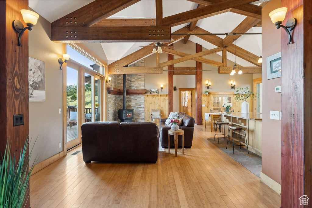 Living room with high vaulted ceiling, ceiling fan, light hardwood / wood-style flooring, and a wood stove