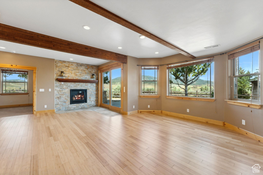 Unfurnished living room with a stone fireplace, beamed ceiling, and light wood-type flooring