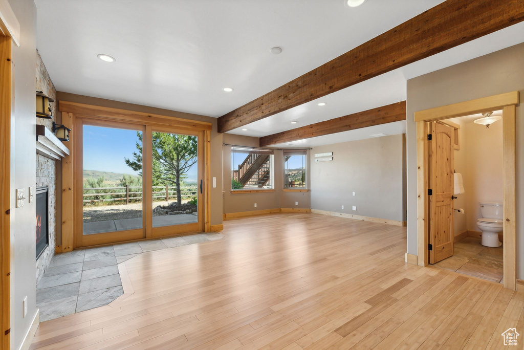 Unfurnished living room featuring a stone fireplace, beamed ceiling, and light hardwood / wood-style flooring